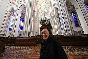 Ein Mann steht in der Kirche. Er lächelt.