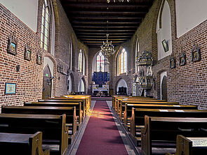 Eine Kirche von innen. Links und rechts stehen Holzbankreihen. Am Ende des Raums befindet sich der Altar.