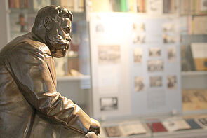 Eine Bronzeskulptur von Reuter. Dahinter, an der Wand, befindet sich eine Glasvitrine mit Infos, Fotos und Büchern.