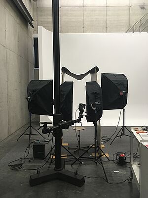 Vor einer weißen Leinwand stehen schwarze Scheinwerfer.