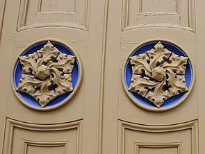Die Tür an der Westfassade trägt auf jedem Flügel ein sandfarbenes Ornament, das in einen blauen Kreis eingelassen ist.