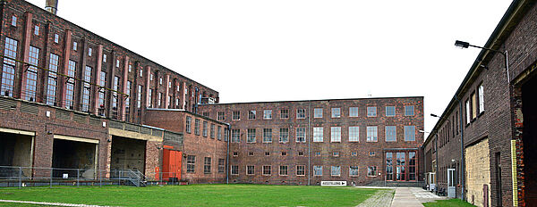 Der Hof des Museums ist an drei Seiten von mehrstöckigen Backsteingebäuden umgeben. Im Hof wächst Wiese und führt ein Weg entlang.