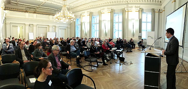 Landrat Sebastian Constien steht in einem Saal am Rednerpult und spricht zu den Zuschauerinnen und Zuschauern.