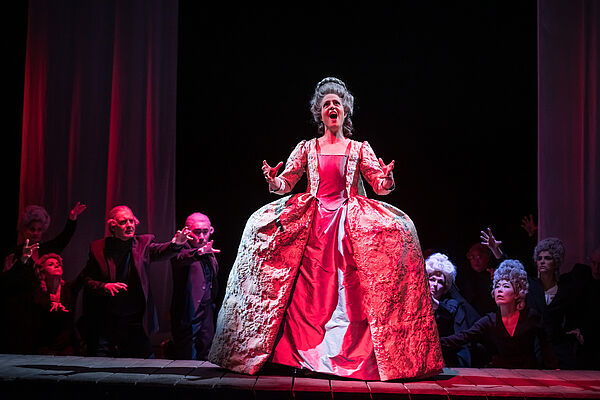 Yvonne Friedli steht in einem langen, roten, königlichen Kleid auf der Bühne und singt.