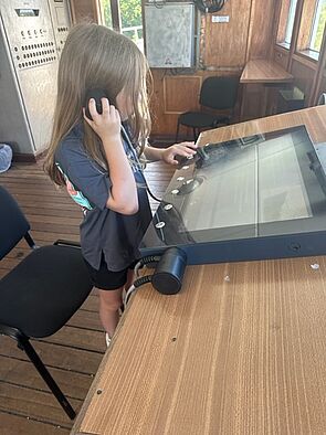 Ein Mädchen hält sich einen Kopfhörer ans Ohr und schaut auf einen Monitor