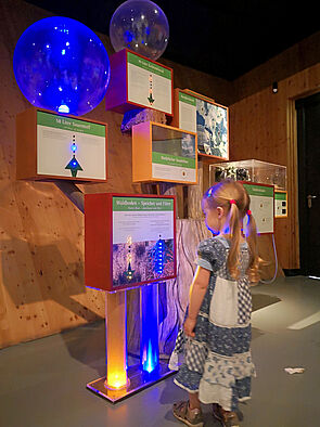 Ein Mädchen steht vor beleuchteten Info-Boxen.