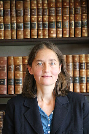 Porträt von Barbara Rimpel. Sie steht vor einem Regal voller historischer Bücher.