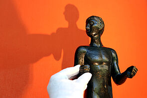 Eine Hand im Handschuh berührt eine Skulptur.