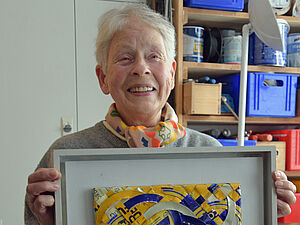 Anka Kröhnke hält einen Bilderrahmen mit einem Kunstwerk in der Hand.