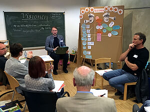 Tino Bittner sitzt vor seiner Seminargruppe. An einer Tafel und einer Pinnwand stehen bzw. hängen die Gedanken, die sie sich an diesem Tag in Bezug auf kulturelle Visionen gemacht haben.