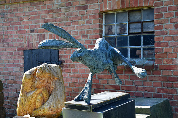 Vor einem Haus, auf einem Sockel, steht eine Hasenskulptur.