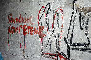 Eine Wand mit roten und schwarzen Strichen. Und einem roten Schriftzug "sinnliche Kompetenz". 