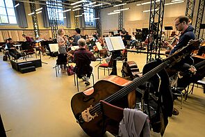 Der Probenraum füllt sich. Einige Musiker sitzen schon an ihren Instrumenten. Andere Stühle sind noch leer.