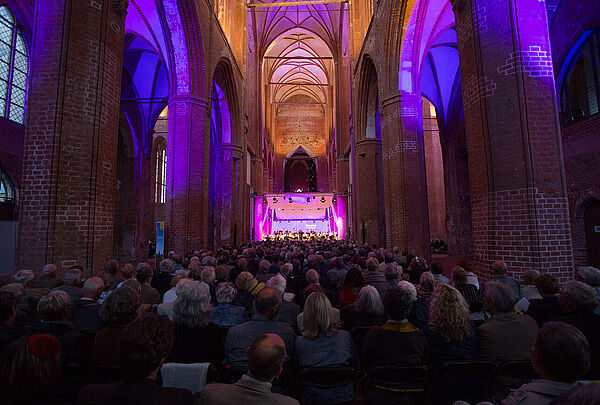Eine Kirche von innen. In der Kirche sitzen viele Menschen. Auf einer Bühne stehen Musiker. Die Bühne ist bunt beleuchtet.
