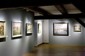 Dicke Holzbalken an der Decke. Darunter an der Wand hängen Bilder.