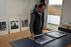 Thomas Häntzschel steht an einem Tisch. Vor ihm liegen zwei Fotografien.