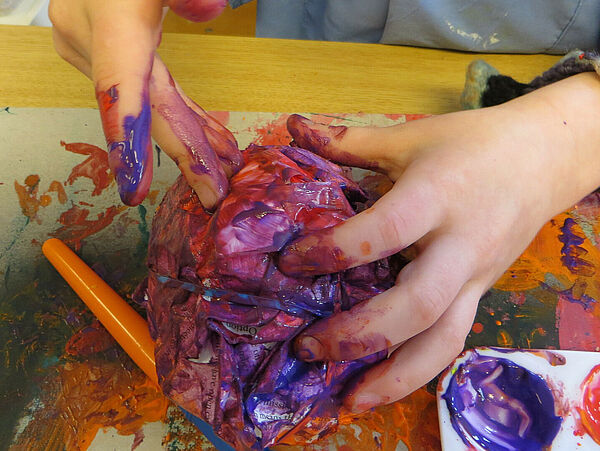 Zwei Hände. Die Finger sind voller Farbe. Die Hände kneten und formen etwas.