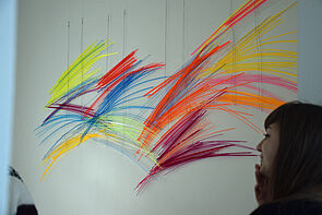 Bunte Stäbe in blau, gelb, rot, orange und violett hängen an einer Wand.