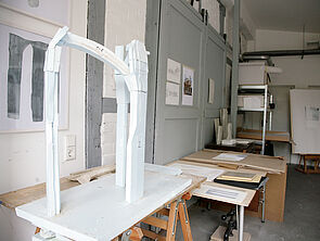 Eine weiße Skulptur aus drei miteinander verbundenen Elementen, die an Säulen erinnern.