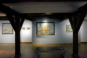 Blick durch den Ausstellungsraum auf ein beleuchtetes Bild.