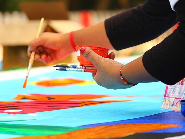 Zwei Hände malen mit einem Pinsel auf einem große Blatt.