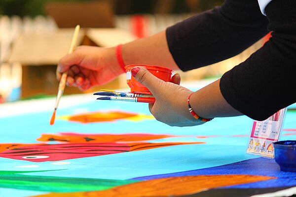Zwei Hände malen mit einem Pinsel auf einem große Blatt.