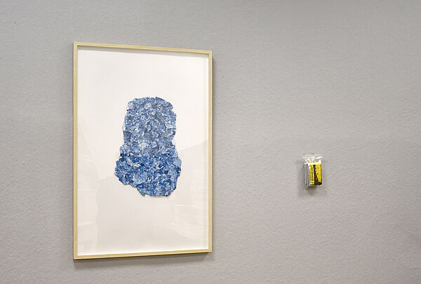 Ein blaues Papier gerahmt hängt an der Wand. Rechts daneben eine gefaltete Rettungsdecke in einer kleinen Tüte.
