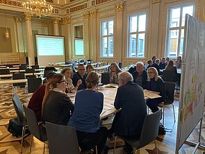 Neun Frauen und Männer sitzen an einem Tisch und reden.