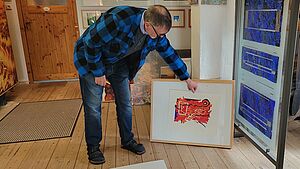 Thomas Kuzio ziegt ein Bild. Das Bild steht neben einer großen Glasmalerei.