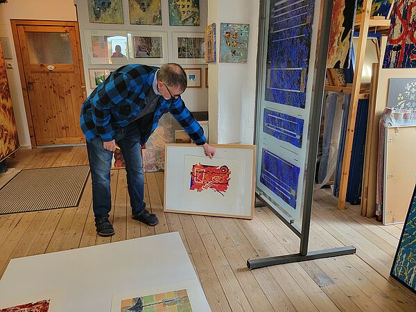 Thomas Kuzio ziegt ein Bild. Das Bild steht neben einer großen Glasmalerei.