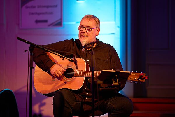 Ein Musiker sitzt am Mikrofon und spielt Gitarre.