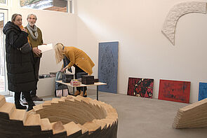 Zwei Frauen, in der Mitte Bruder Burow in einem Atelier. Sie begutachten Arbeiten des Künstlers.