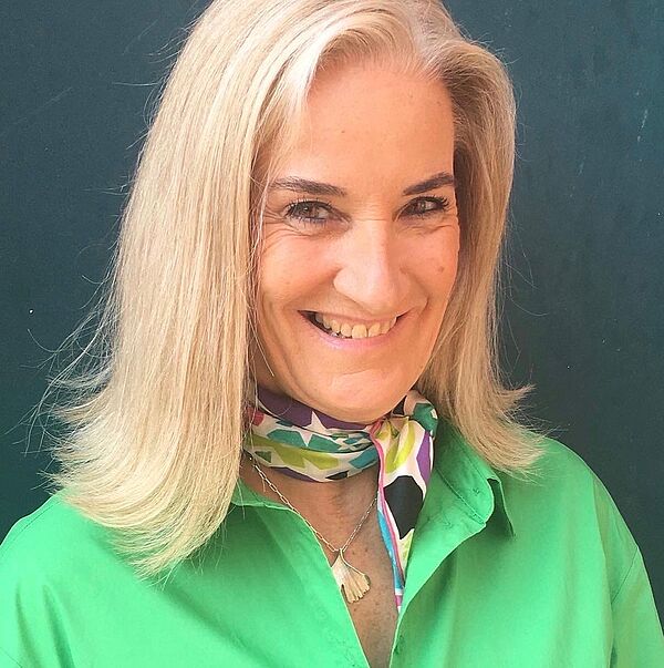 Porträt einer Frau. Sie hat blonde, halblange Haare und trägt ein grünes Hemd.