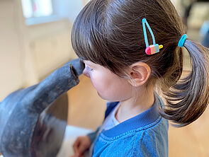 Ein Mädchen schaut wie bei einem Mikroskop durch eine Plastik.