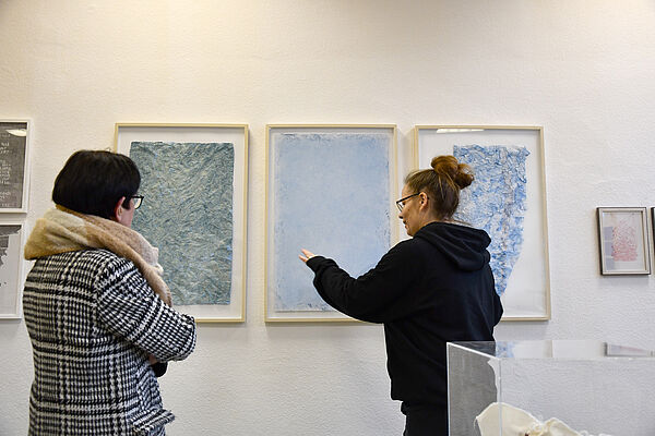 Ramona Seyfarth zeigt auf drei eingerahmte Papiere aus ihrer Serie Trans_Plantation.