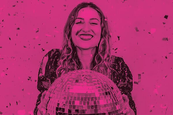 Eine Frau im Konfettiregen hält eine Diskokugel.