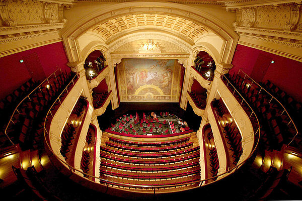 Vom obersten Rang fällt der Blick nach unten auf die Bühne, den Orchestergraben und die Zuschauerreihen im Parkett.