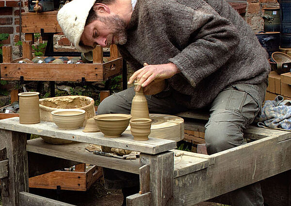Ein Mann sitzt an einer Töpferscheibe und töpfert eine Vase.